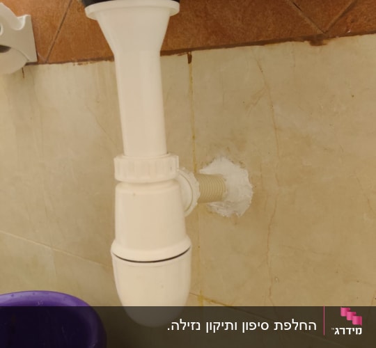 צינור ניקוז לבן מתחת לכיור עם דלי סגול